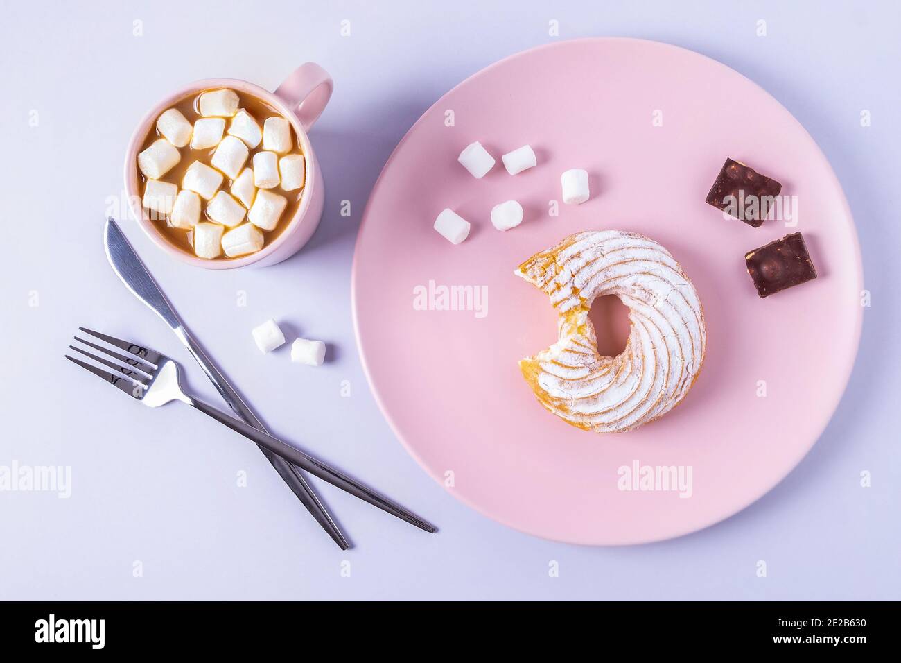 Top view still life of a bitten cake on a pink plate, cutlery and a cup of cocoa with marshmallows. Selective focus, horizontal orientation. Stock Photo