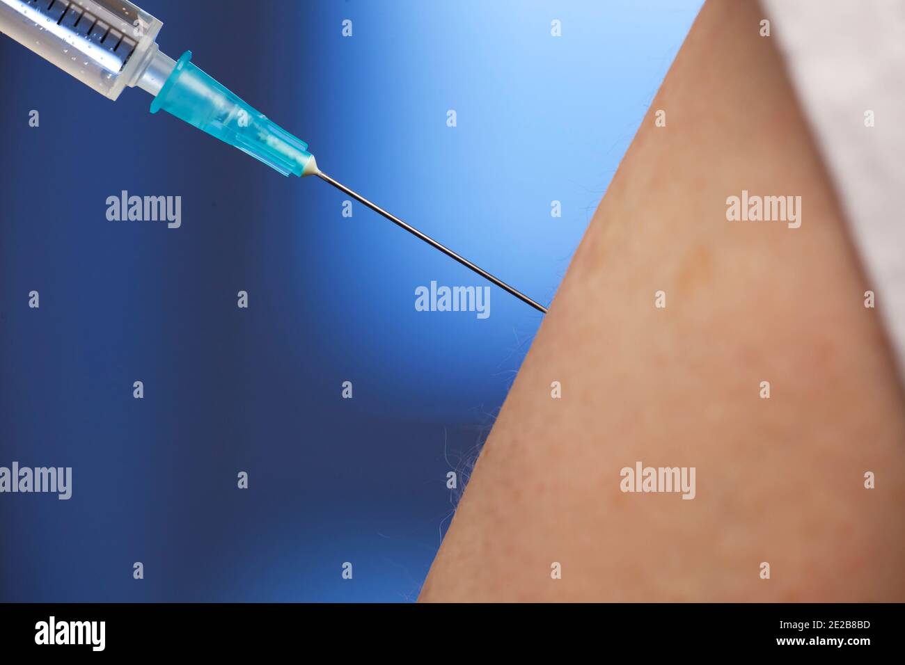 Close-up of vaccination with syringe in upper arm - focus on the needle - blue background Stock Photo
