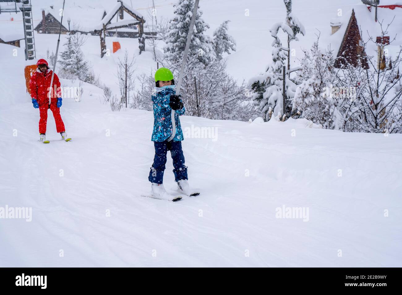 AURON, FRANCE-01.01.2021: Professional ski instructor and child lifting on the ski drag lift rope to the mountain during snowfall. Family and children active vacation concept. Blurred focus background Stock Photo