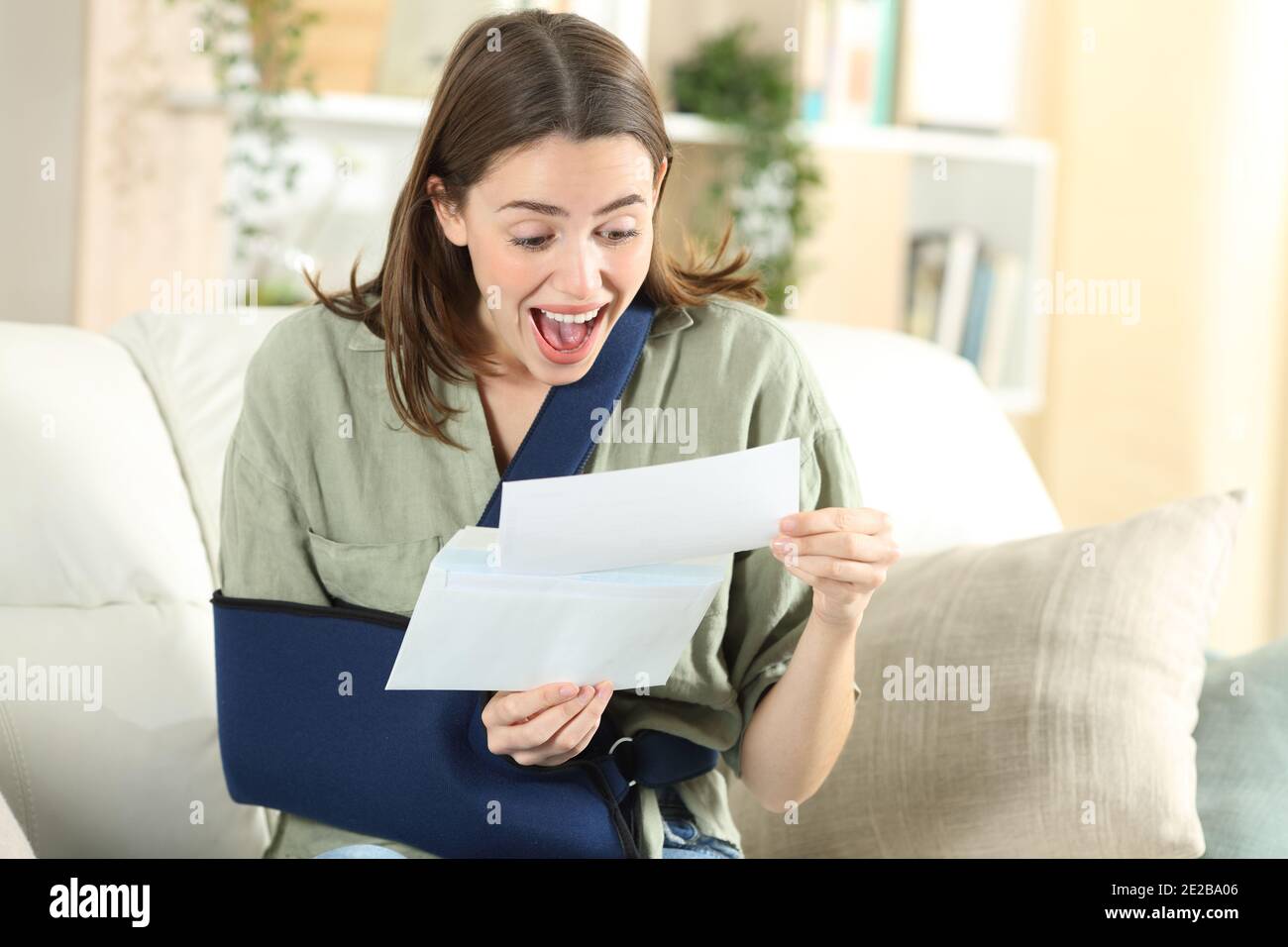 Excited disabled woman receiving good news on letter sitting on a couch in the living room at home Stock Photo