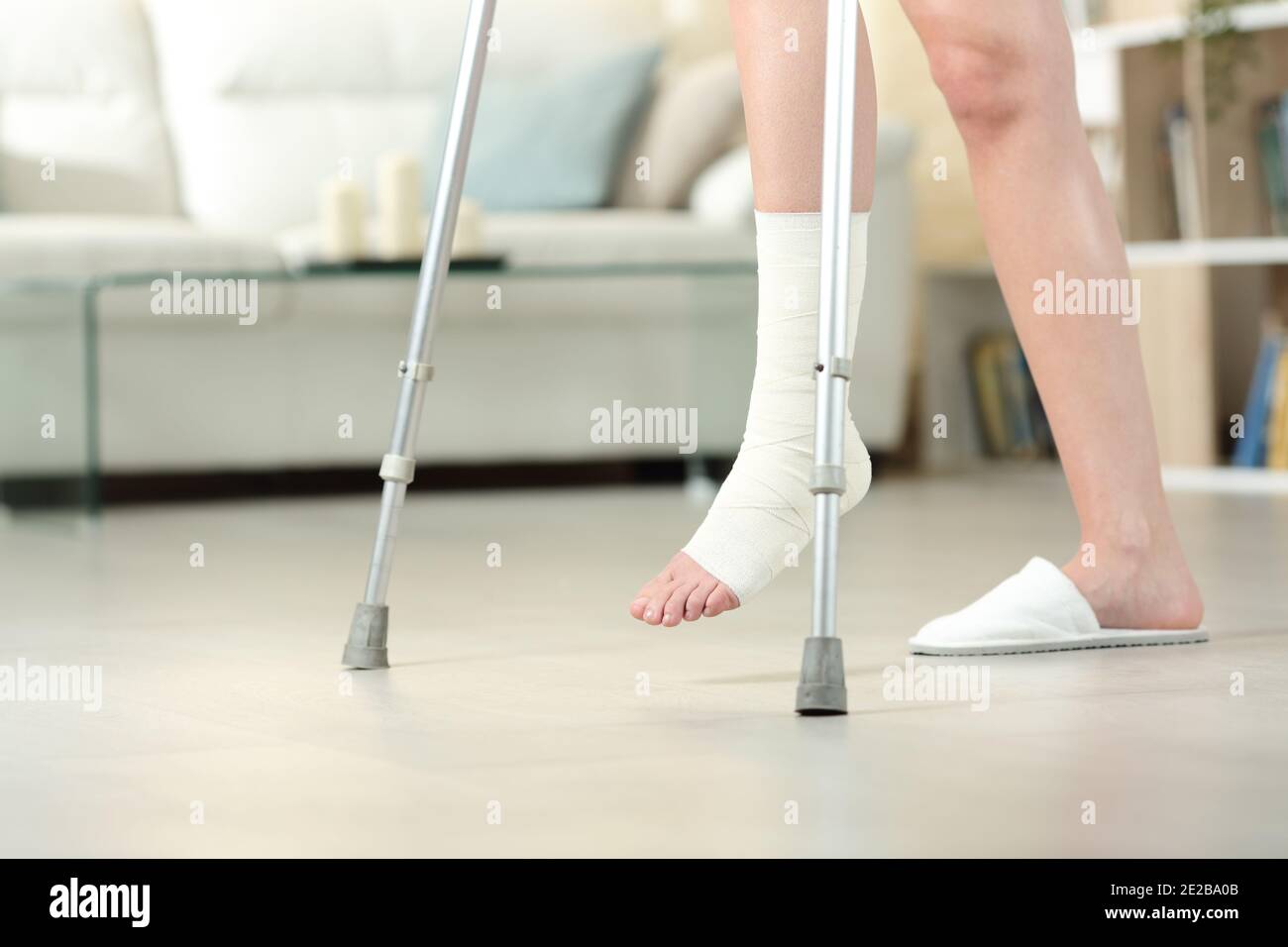 Side view portrait of a disabled woman with bandaged foot walking with crutches at home Stock Photo
