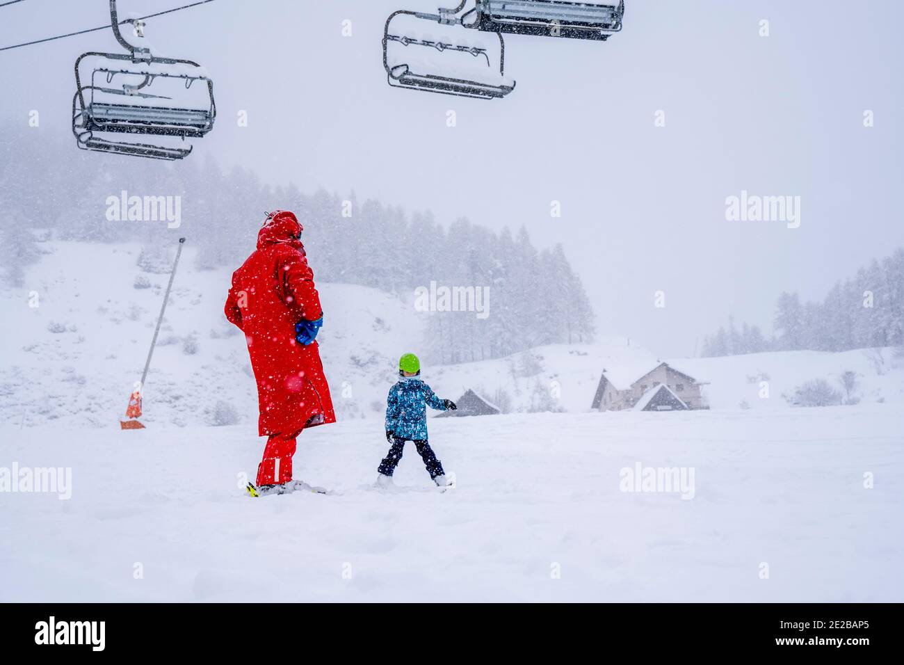 Professional ski instructor is teaching a child to ski on a mountain slope. Snowfall day. Family and children active vacation concept. Blurred focus background.  Stock Photo