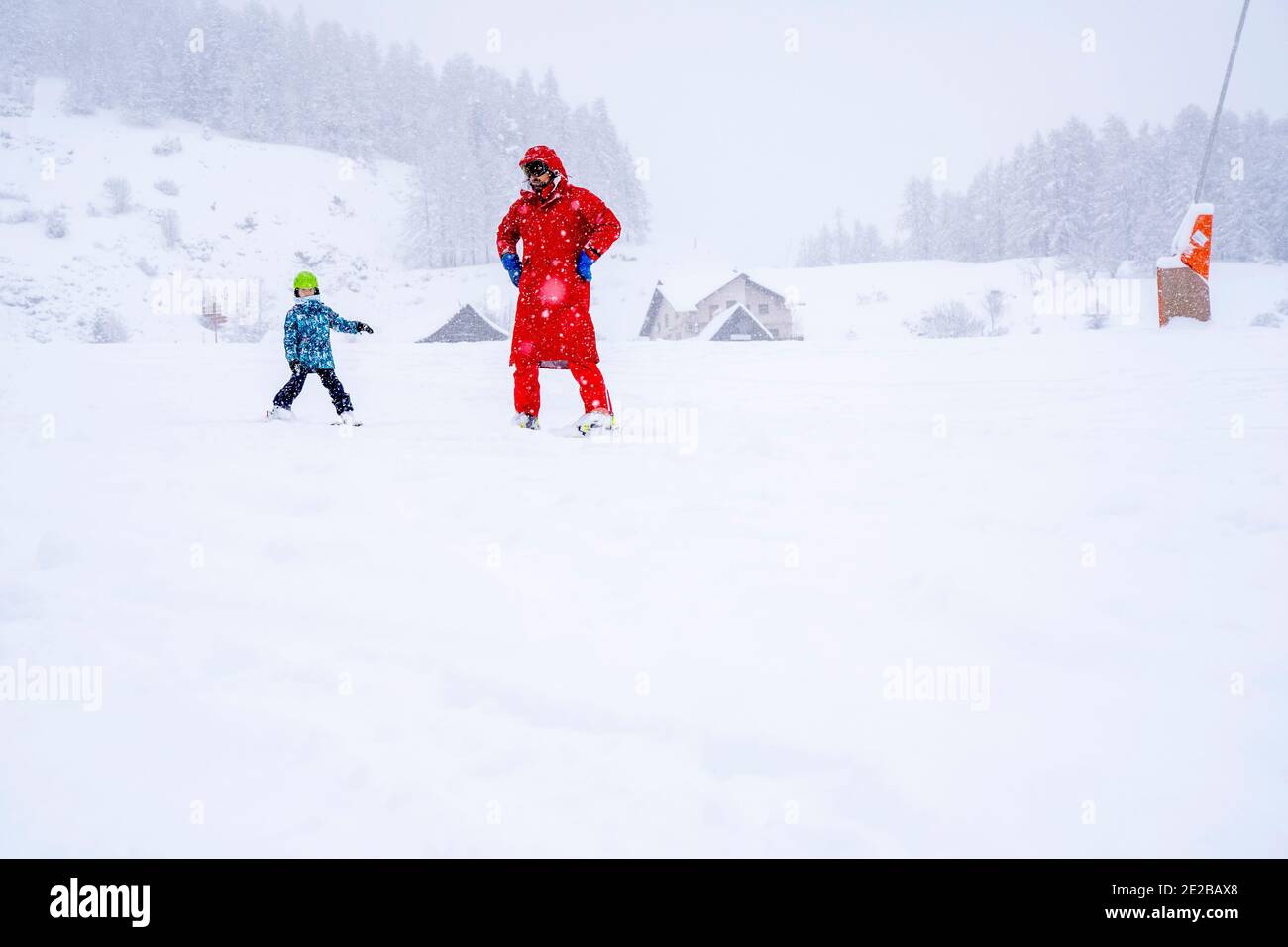AURON, FRANCE- 01.01.2021: Professional ski instructor is teaching a child to ski on a mountain slope. Snowfall day. Family and children active vacation concept. Blurred focus background.  Stock Photo