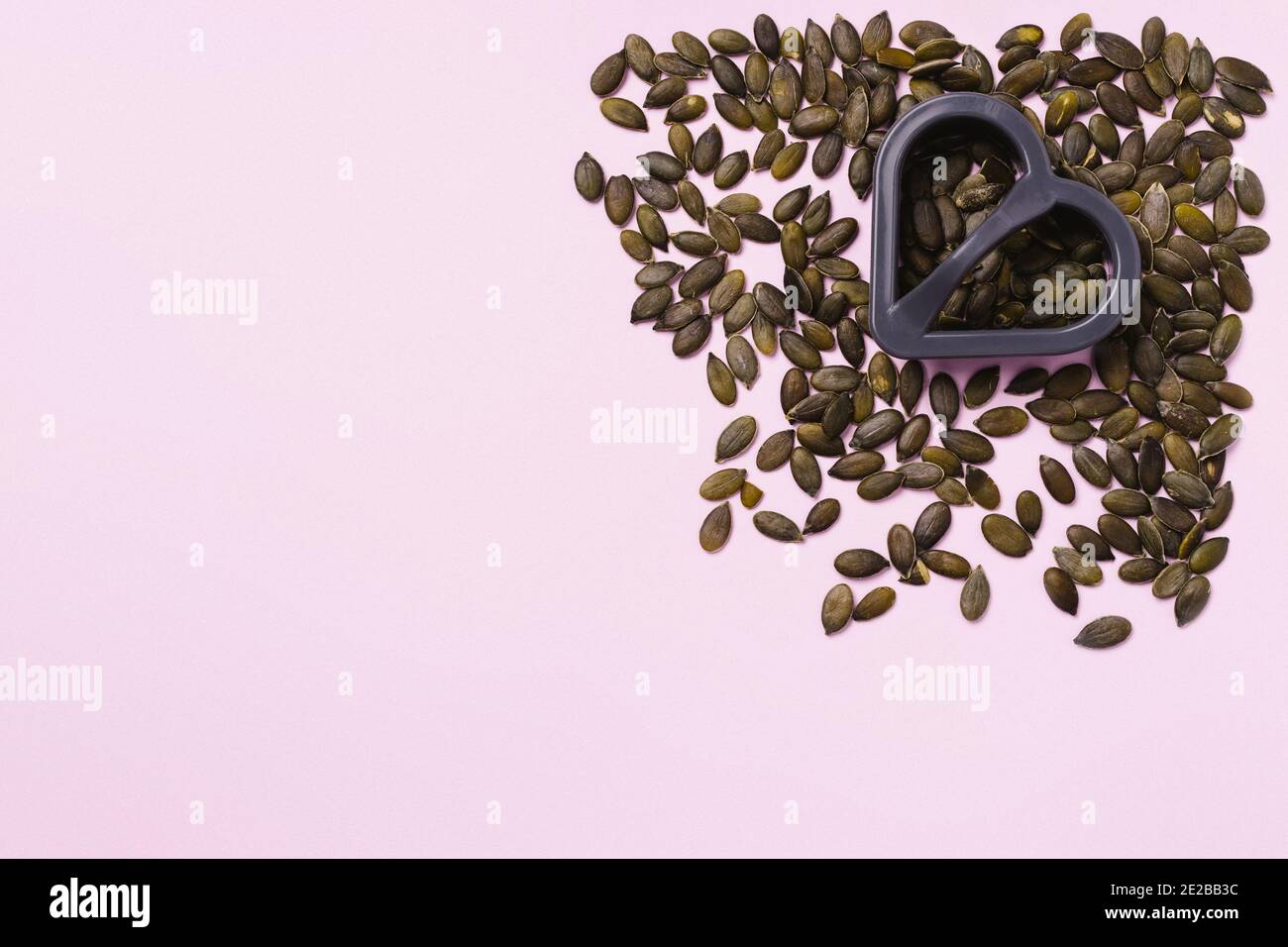 Pink background. Pumpkin seeds in the right corner and a heart-shaped cookie cutter. Empty space for advertising. Stock Photo