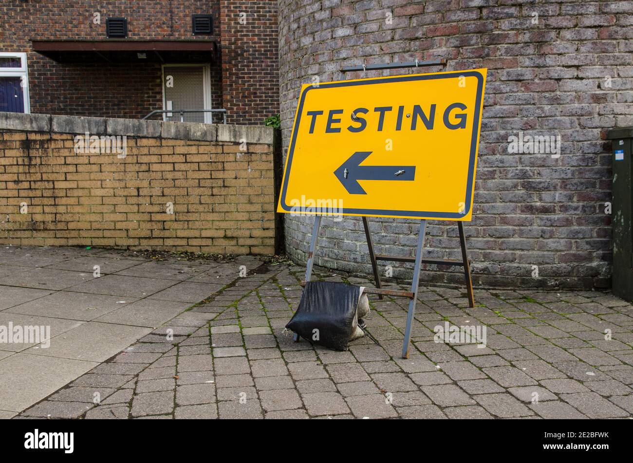 A direction sign for pedestrians pointing in the direction of a COVID testing centre against an annonymous brick wall. Stock Photo