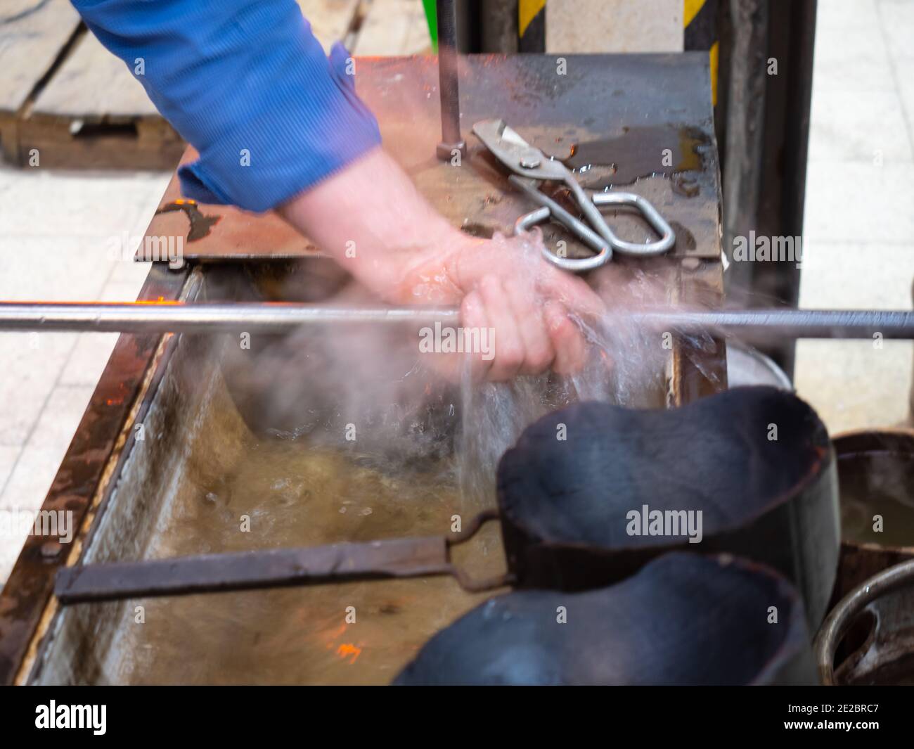 Glassblower is cooling the hot blowing pipe. Turning with whistle to
