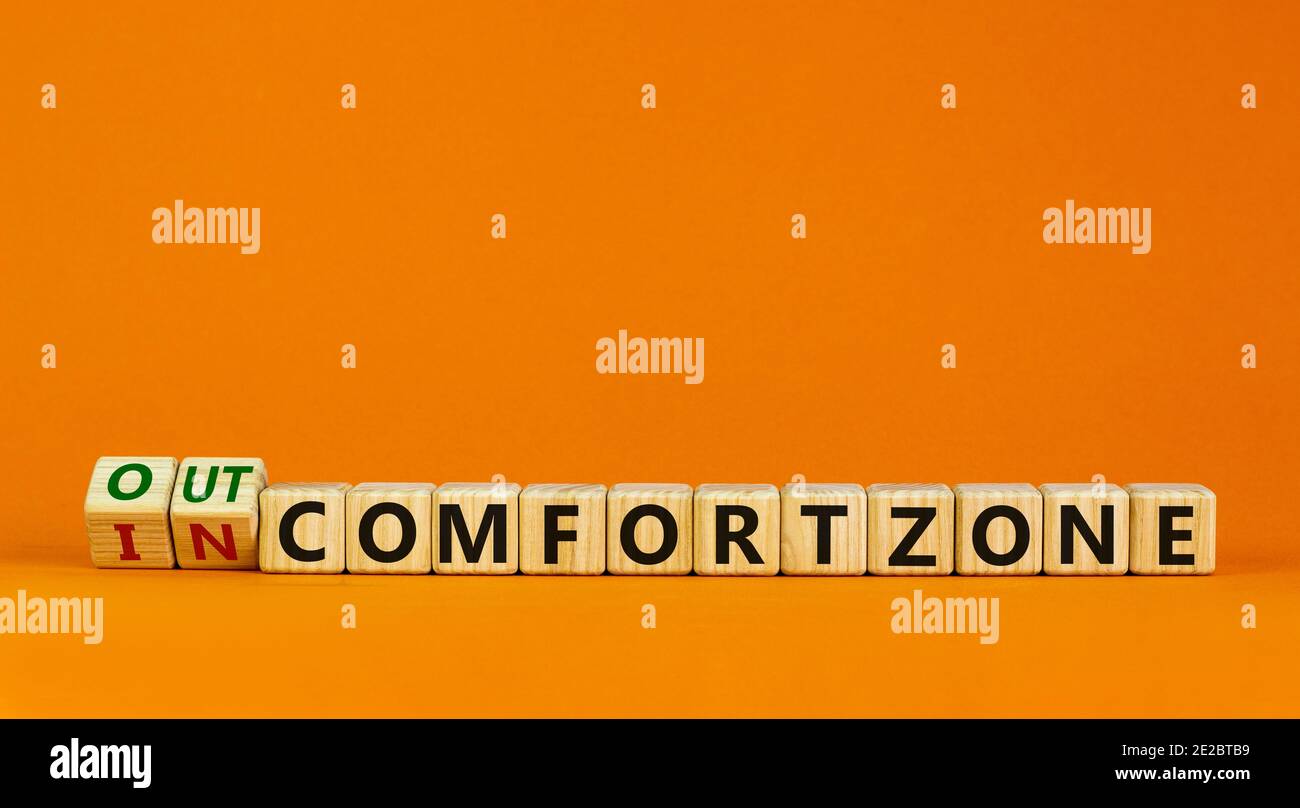 Out or in comfort zone symbol. Turned wooden cubes and changed words 'in comfort zone' to 'out comfort zone'. Beautiful orange background, copy space. Stock Photo