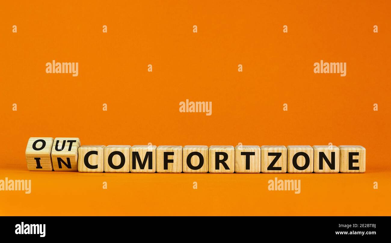 Out or in comfort zone symbol. Turned wooden cubes and changed words 'in comfort zone' to 'out comfort zone'. Beautiful orange background, copy space. Stock Photo