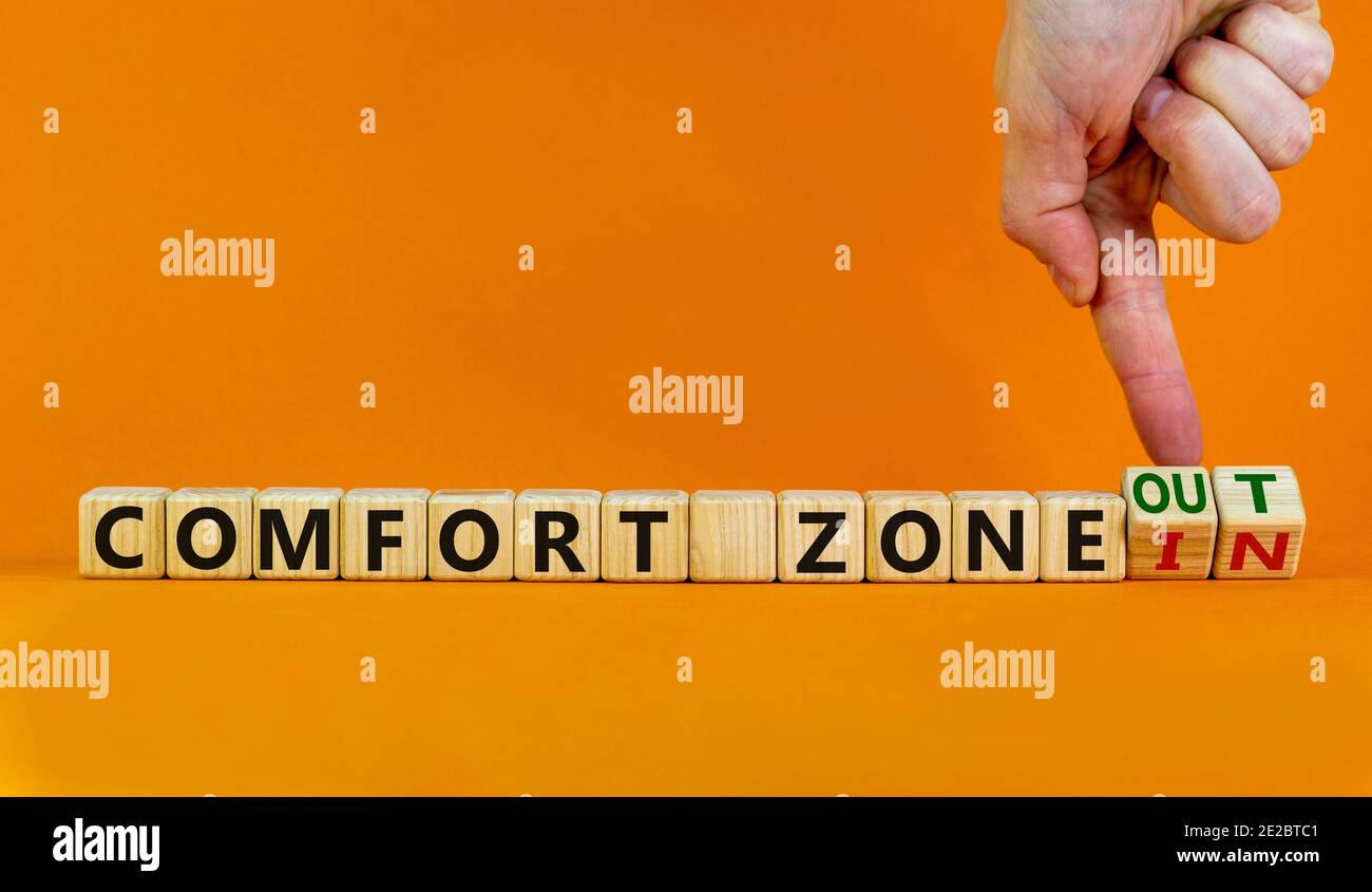 Out or in comfort zone symbol. Hand turns wooden cubes and changes words 'in comfort zone' to 'out comfort zone'. Beautiful orange background, copy sp Stock Photo
