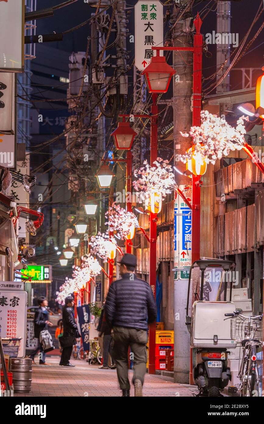 TOKYO, JAPAN - MARCH 20, 2014: A pedestrian passes through an lleyway in Shinjuku  with decorative spring ornaments at night. Stock Photo
