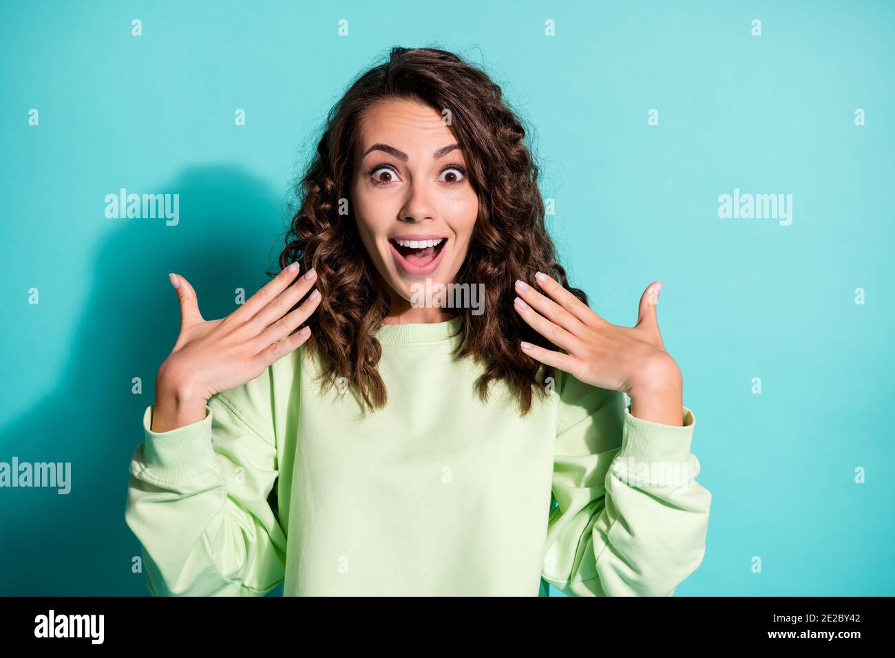 Portrait of astonished young woman dressed casualwear green pullover raise hands isolated on turquoise color background Stock Photo