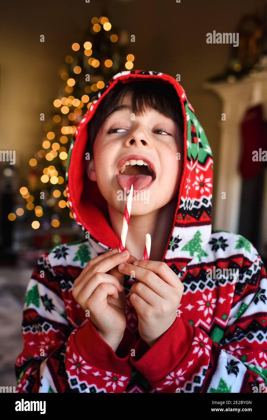 Cute boy in festive pajamas eating a candy cane at christmas time Stock