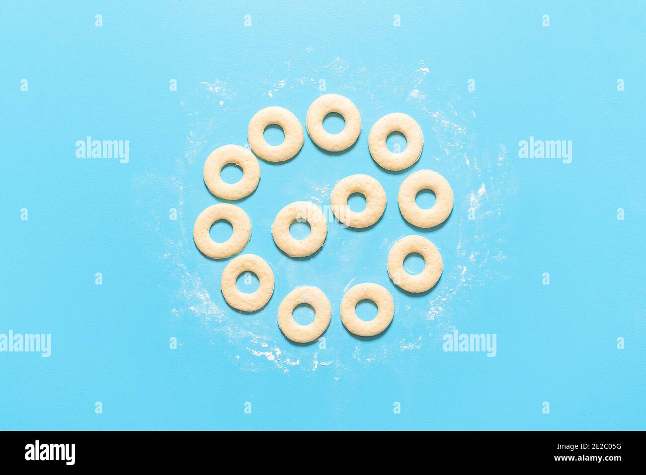 Raw donut dough cut in ring shapes, on blue background. Cooking doughnuts recipe. Homemade yeast raised donuts. Uncooked sweet dough. American sweets. Stock Photo