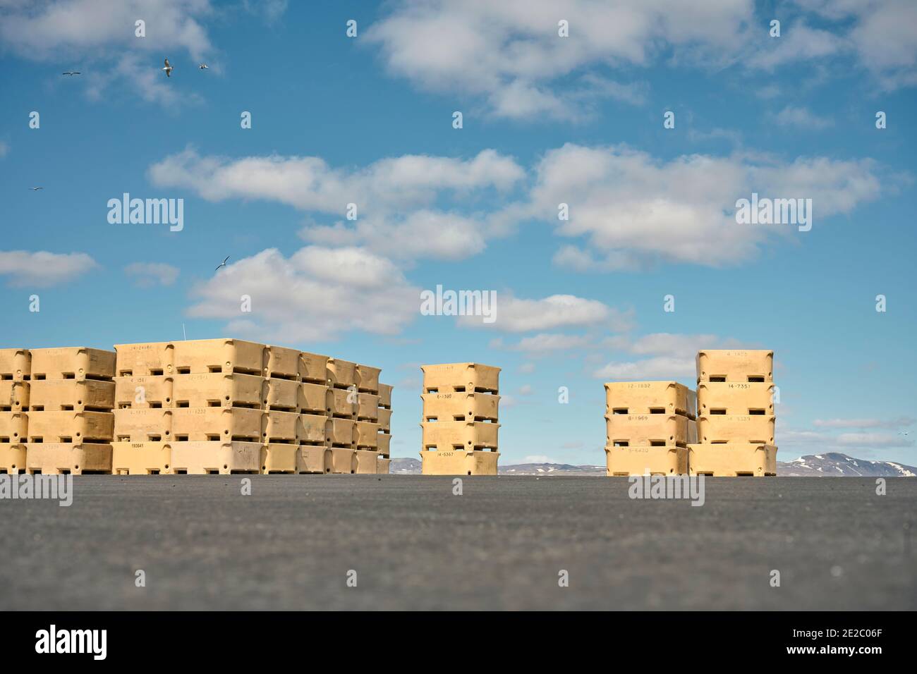 Stacks of fish storage containers stacked on ground against cloudy blue sky on sunny day in countryside Stock Photo