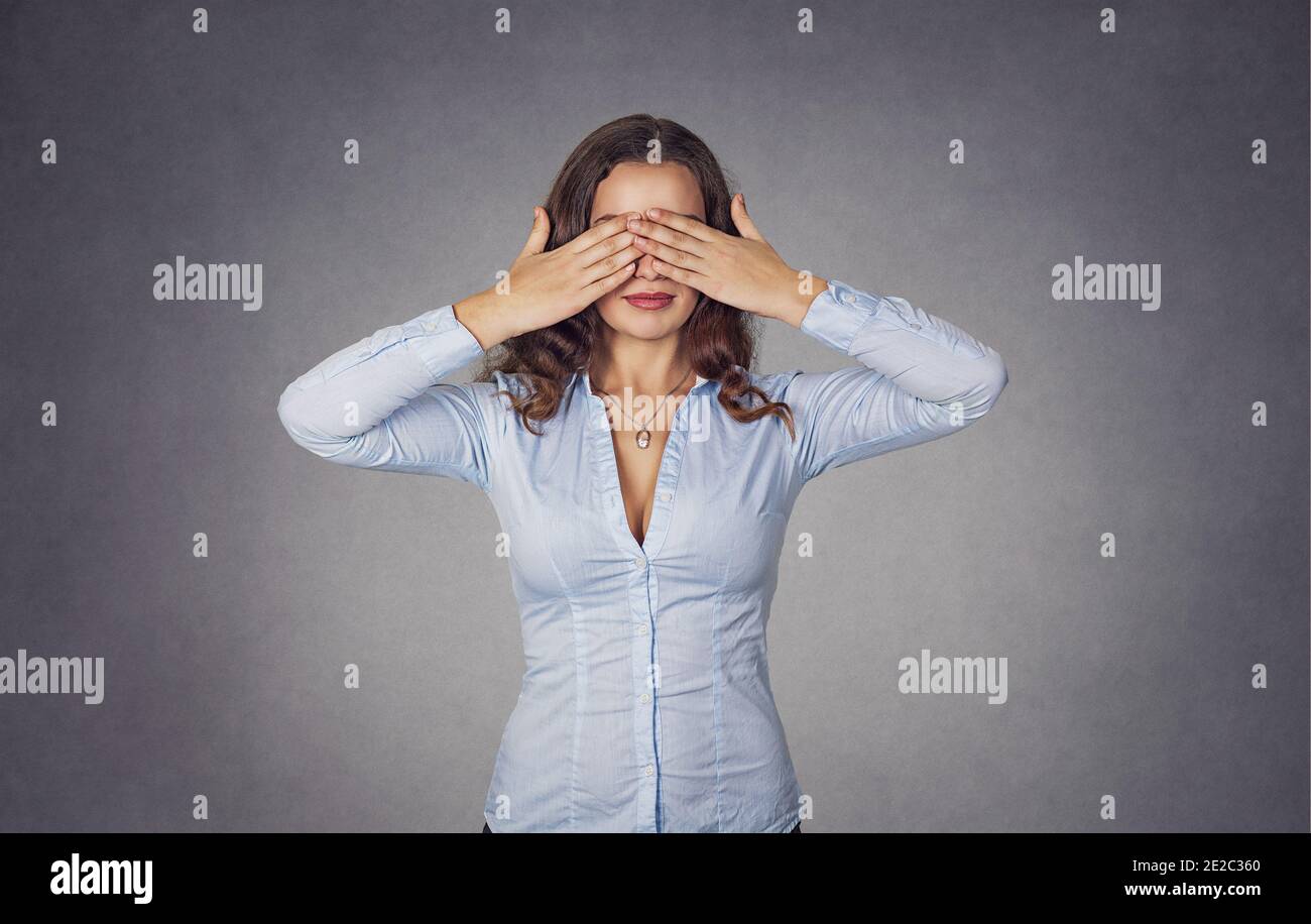Beautiful young woman covers eyes with hands. Closeup portrait of a beautiful girl in blue formal shirt isolated over gray background. Mixed race, his Stock Photo