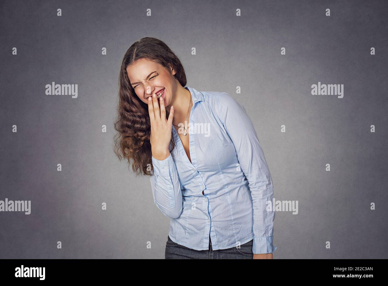 Beautiful smiling shy woman covering teeth with hand, girl with clean skin, natural make-up laughing happy isolated on studio gray background. Model g Stock Photo