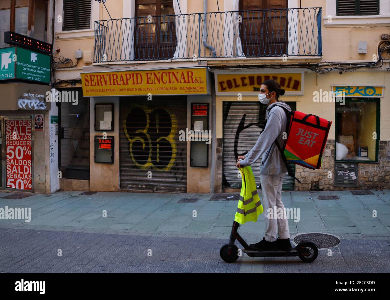 Palma De Mallorca, Spain. 13th Jan, 2021. A young employee of the company Just Eat drives his scooter past closed shops. Since Jan. 13, 2021, all restaurants, cafes and bars on the Spanish holiday islands, as well as all gyms and large stores that do not cover basic needs, must remain closed. Deliveryando parent Just Eat Takeaway has benefited significantly from the trend towards online food ordering in the Corona year 2020. Credit: Clara Margais/dpa/Alamy Live News Stock Photo