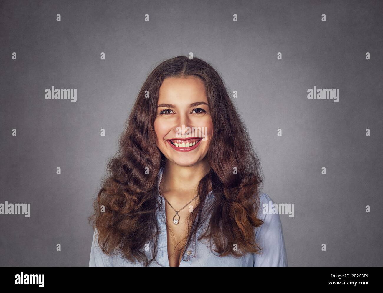 Closeup young woman with wavy hair showing toothy smile isolated on gray wall background. Positive face emotion. Stock Photo