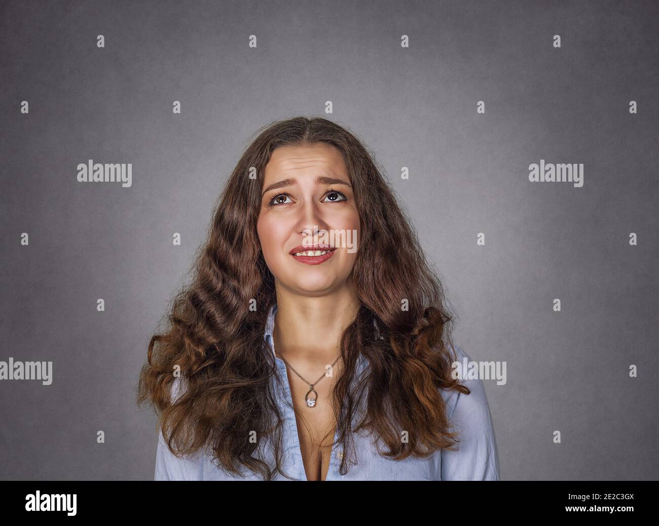 closeup portrait headshot cute unhappy woman looking up isolated on gray wall background with copy space above head. Human face expressions, emotions. Stock Photo