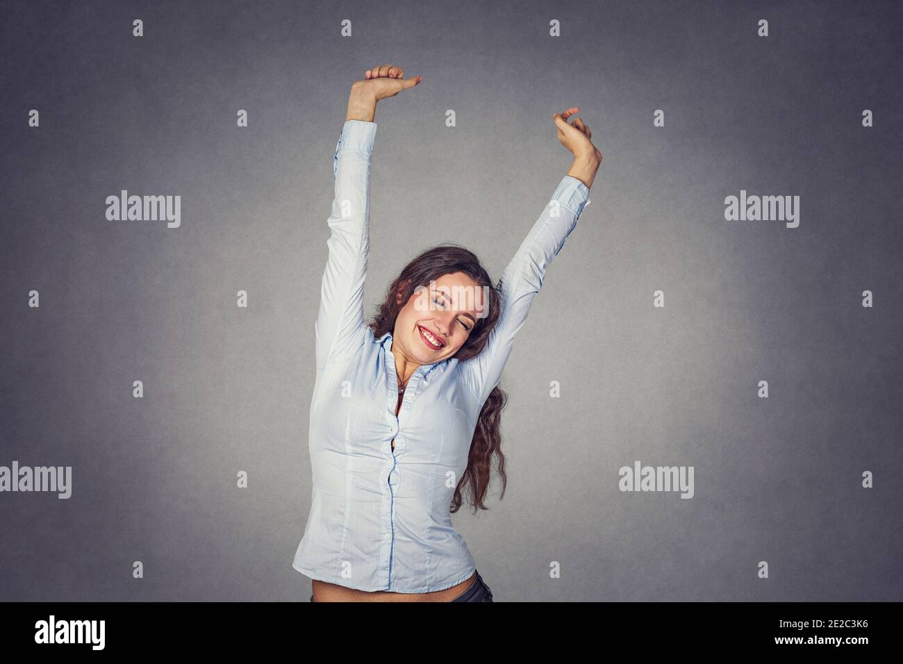 Happy smiling young woman stretching her arms wearing formal blue shirt stretching isolated on gray background. Stock Photo
