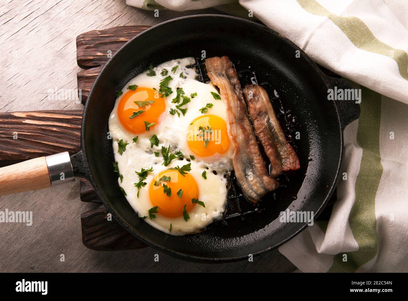 Scrambled eggs and bacon in a small pan on the kitchen table Stock Photo