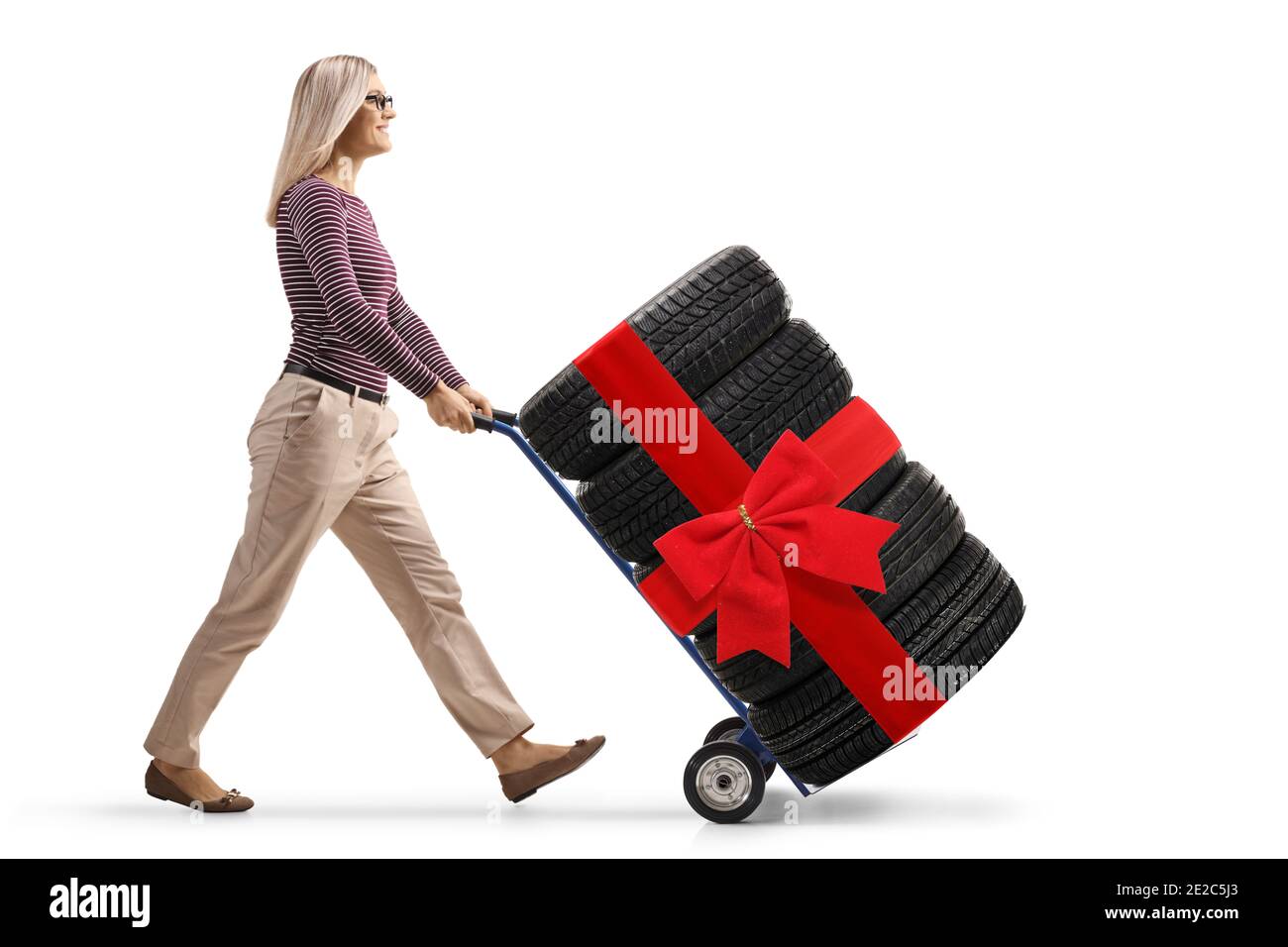 Full length profile shot of a young woman pushing a hand-truck loaded with tires tied with a red ribbon isolated on white background Stock Photo