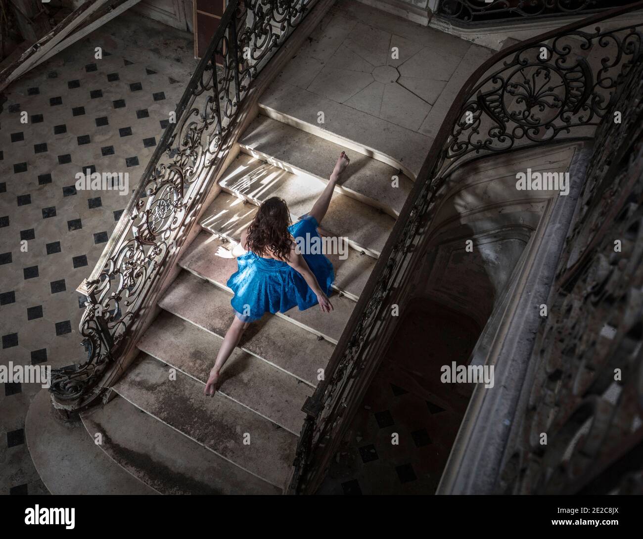 Gymnastic girl in blue dress doing the splits on staircase in Chateau de Singes Stock Photo