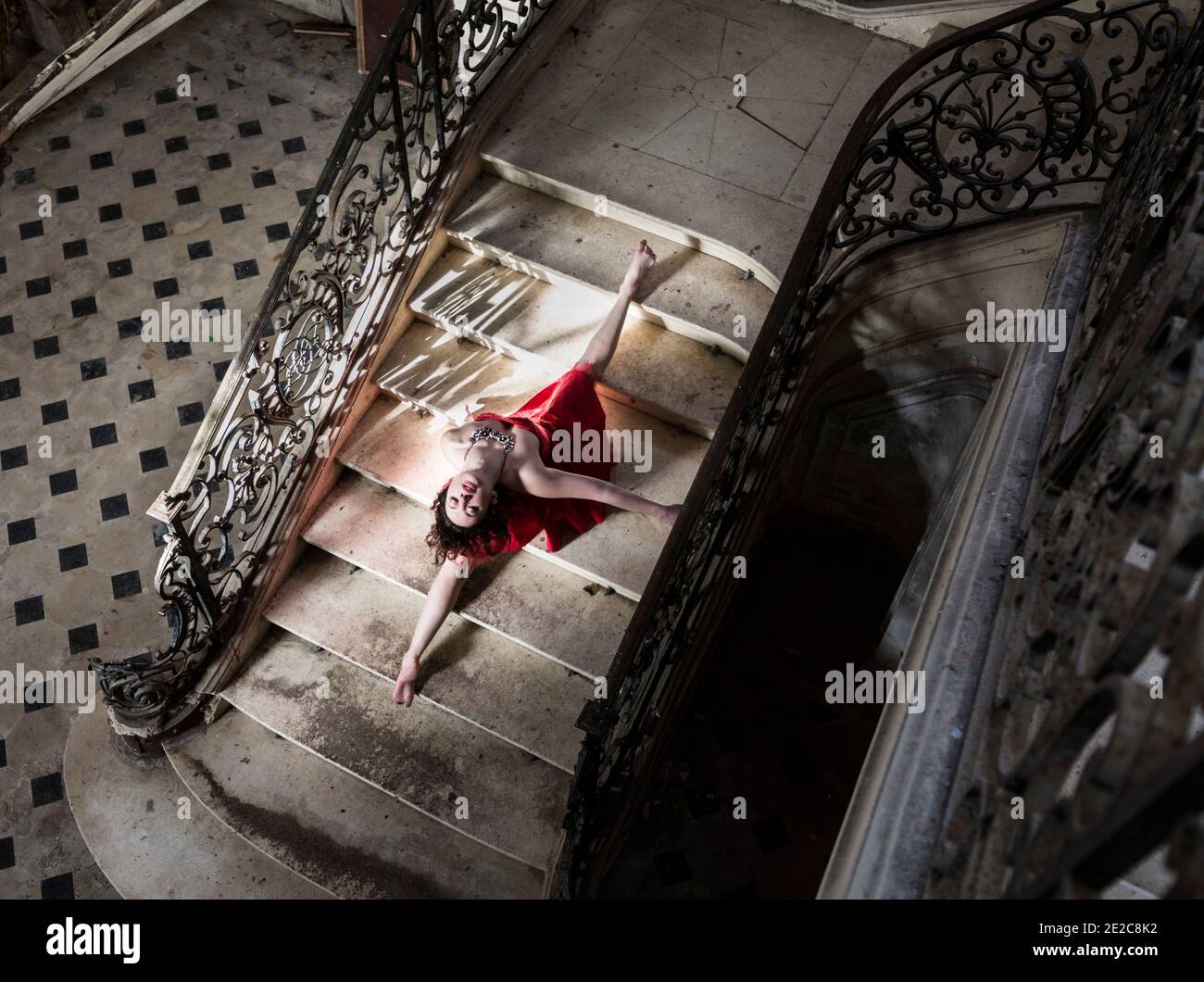 Gymnastic girl in red dress doing the splits on staircase in Chateau de Singes Stock Photo