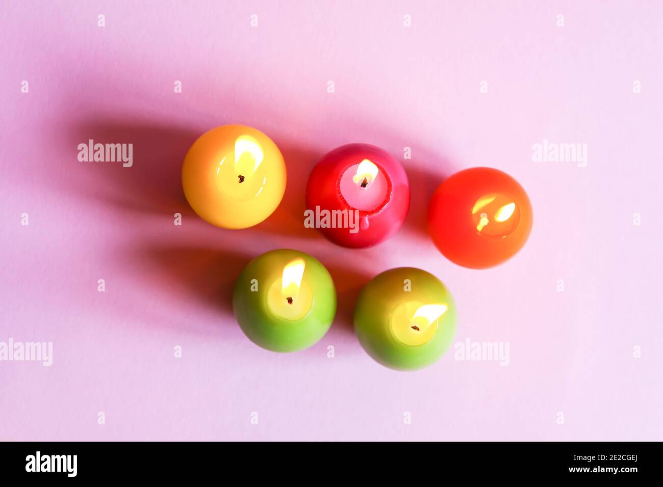 Traditional Easter decor. Group of bright burning paraffin candles in the shape of colorful eggs on soft pink background. Stock Photo