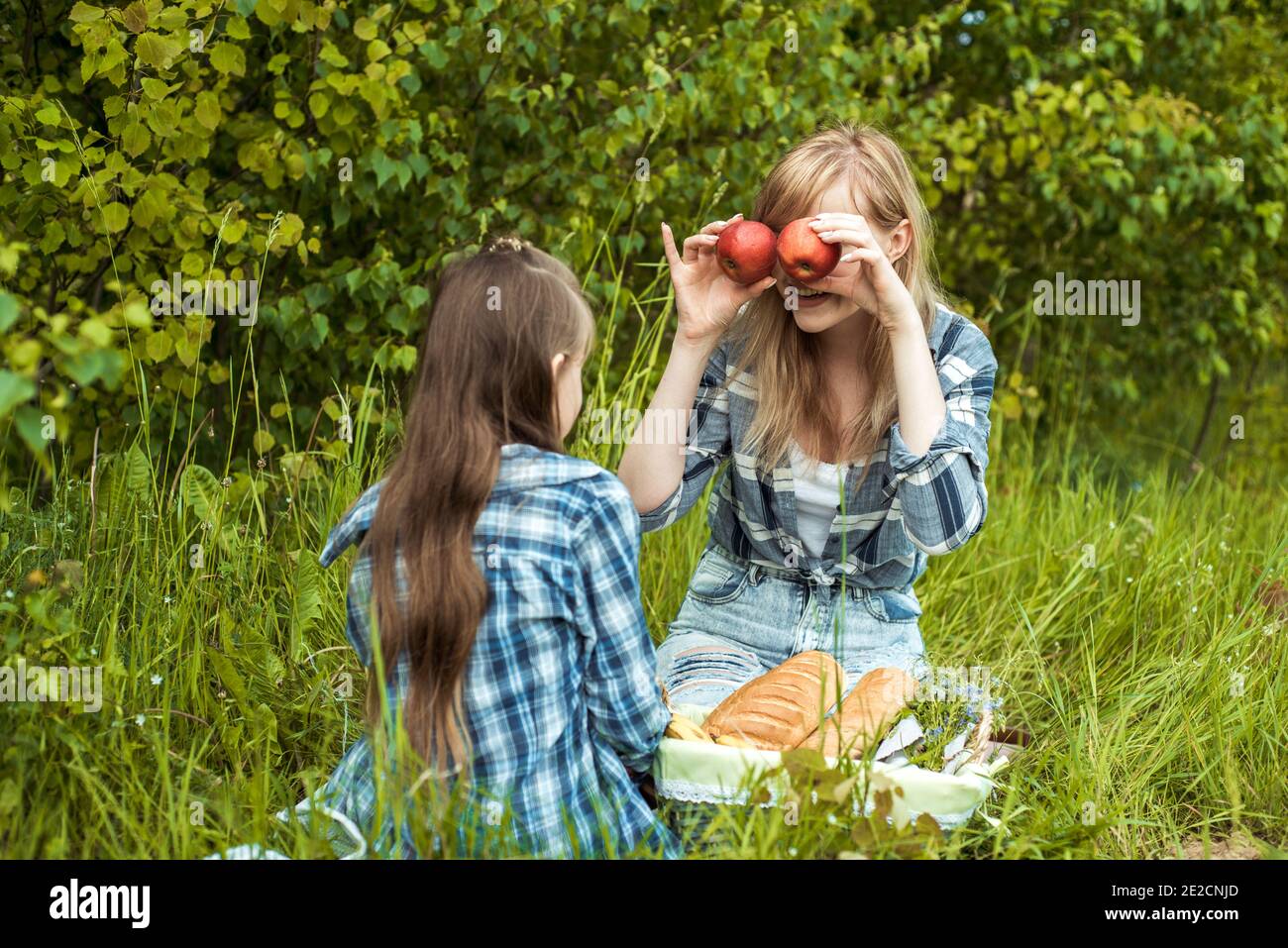 Happy smiling woman and fun enjoying kid, mother holding the red apples near the eyes.Picnic in the park, happy family. Sunny summer day outdoors Stock Photo