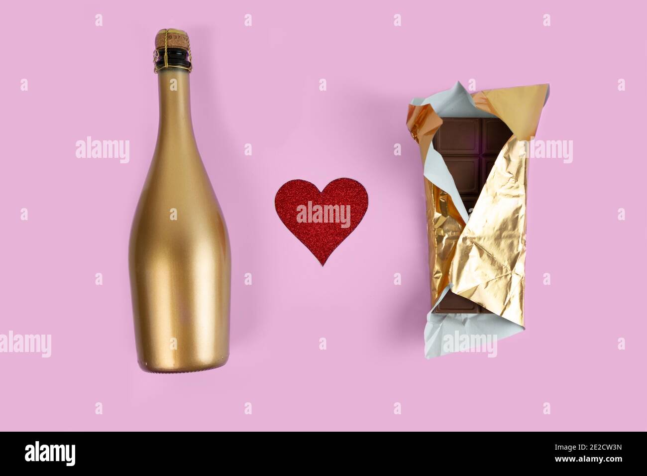 Golden champagne bottle and chocolate bar in gold wrapper and red glitter heart on a pink