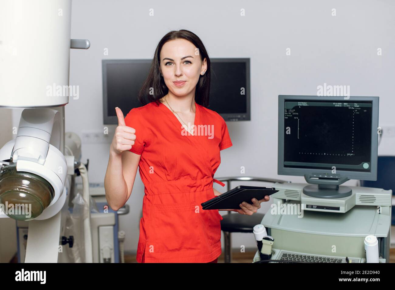 Close up of pretty Caucasian woman doctor standing in front of ultrasound and lithotripter machines and showing thumb up. Safety non-invasive stone Stock Photo