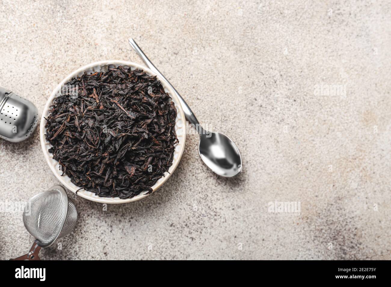 Dry black tea leaves in bowl and infusers on light background Stock