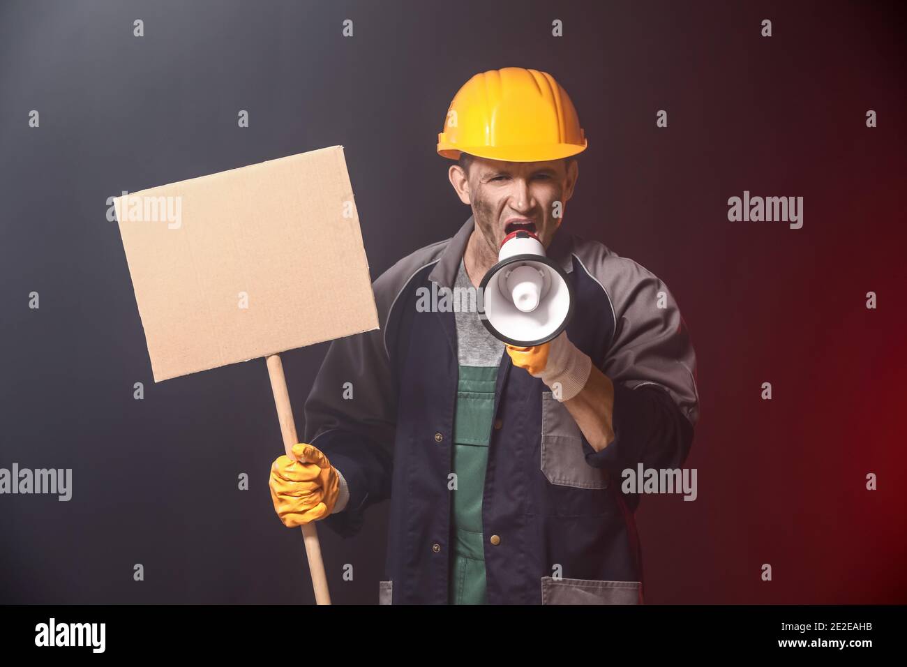 Protesting miner man with megaphone and placard on dark background Stock Photo