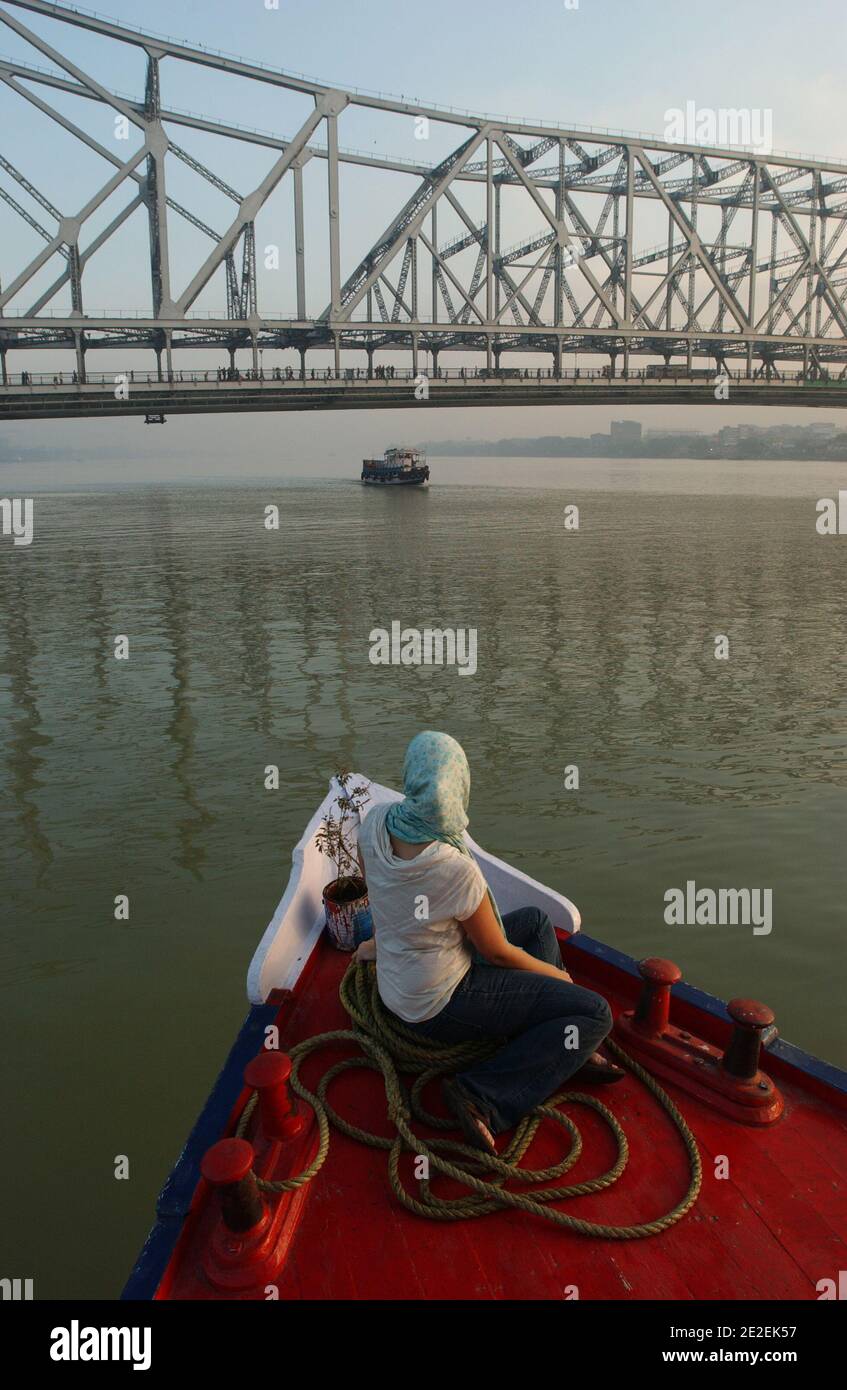 The Howrah Bridge, crosses the river Hooghly one of the longest bridges in the world (about 150 000 vehicles and 4,000 pedestrians cross it each day). Woman sitting in the front of a boarding( ship/boat ), Kolkata, India, 2007.Le pont Howrah, franchit la riviere Hooghly un des plus longs ponts du monde( environ 150 000 voitures et 4 000 pietons le traversent chaque jours ). Femme assise a l'avant d'une embarquation( barque/bateau), Calcutta, Inde, 2007. Photo by David Lefranc/ABACAPRESS.COM Stock Photo