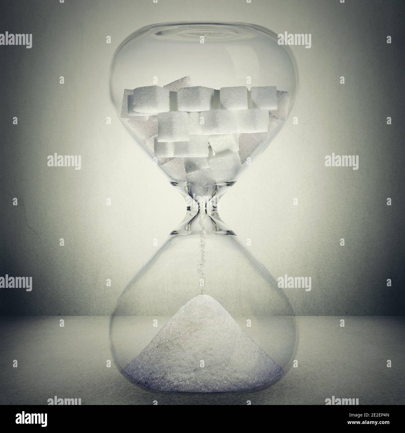 Sugar kills in time, death concept. Closeup of hourglass with sugar in cubes that is pouring down transforms into powder isolated on gray background Stock Photo