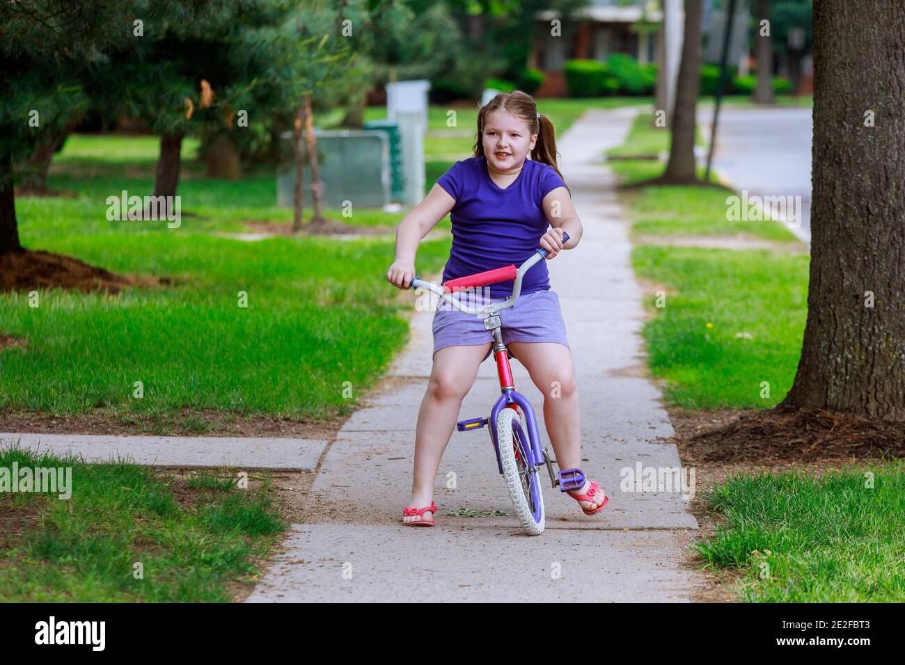 Beautiful little girl smiling is riding the bicycle in the park on a city Stock Photo