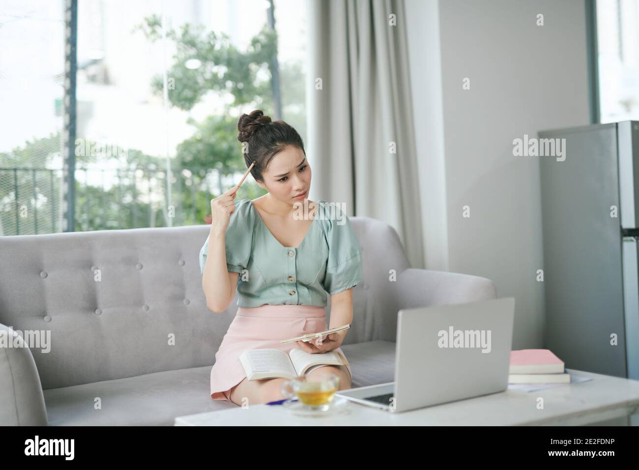 Thoughtful woman using laptop, looking aside while sitting on cozy sofa. Mature female thinking about new working project Stock Photo