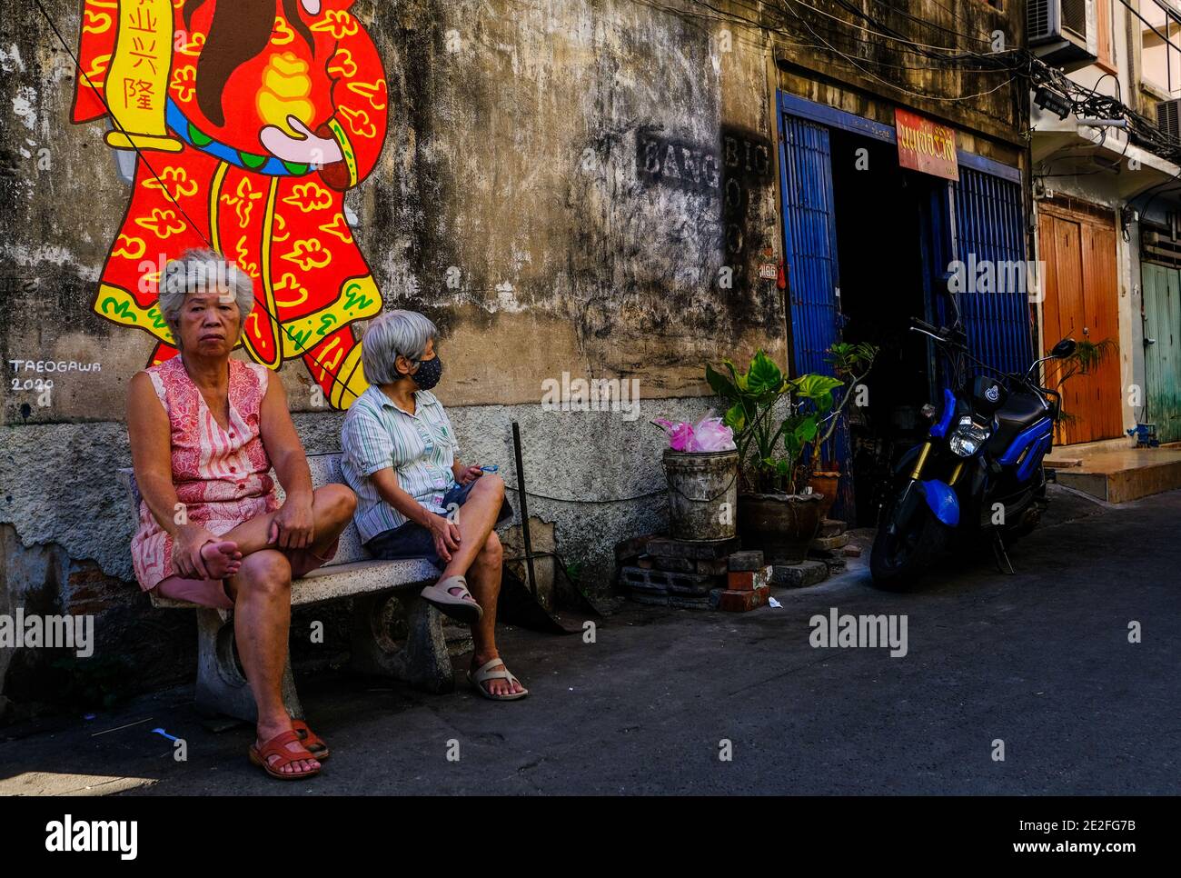 Two elderly Chinese ladies sit on a bench in an alley in Talat Noi, Bangkok Stock Photo