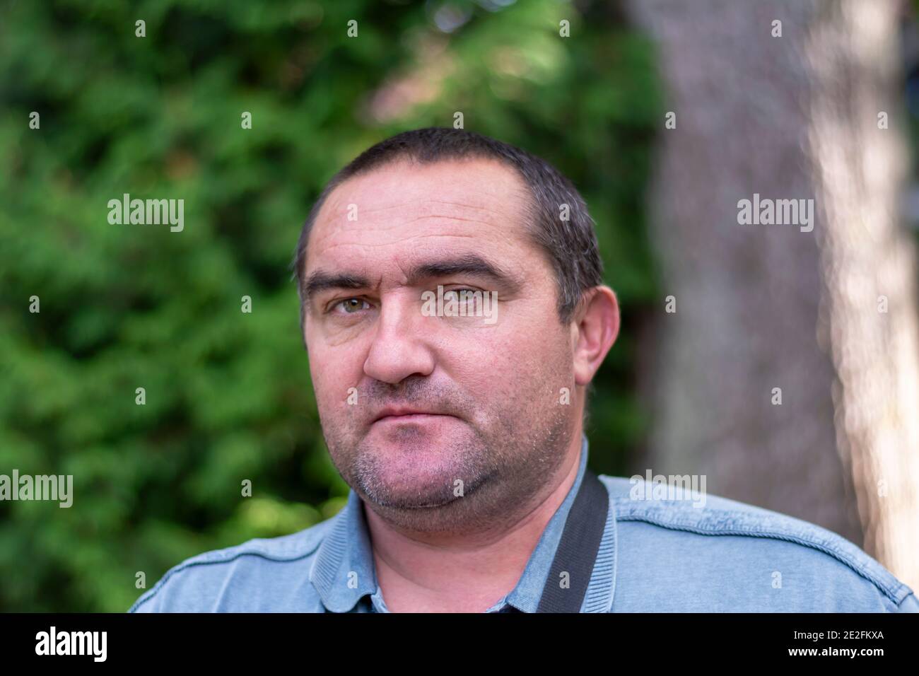 Caucasian white male 40 years old with stubble on his face posing outdoors in summer. Portrait of bristly man in street. Selective focus, blurred back Stock Photo