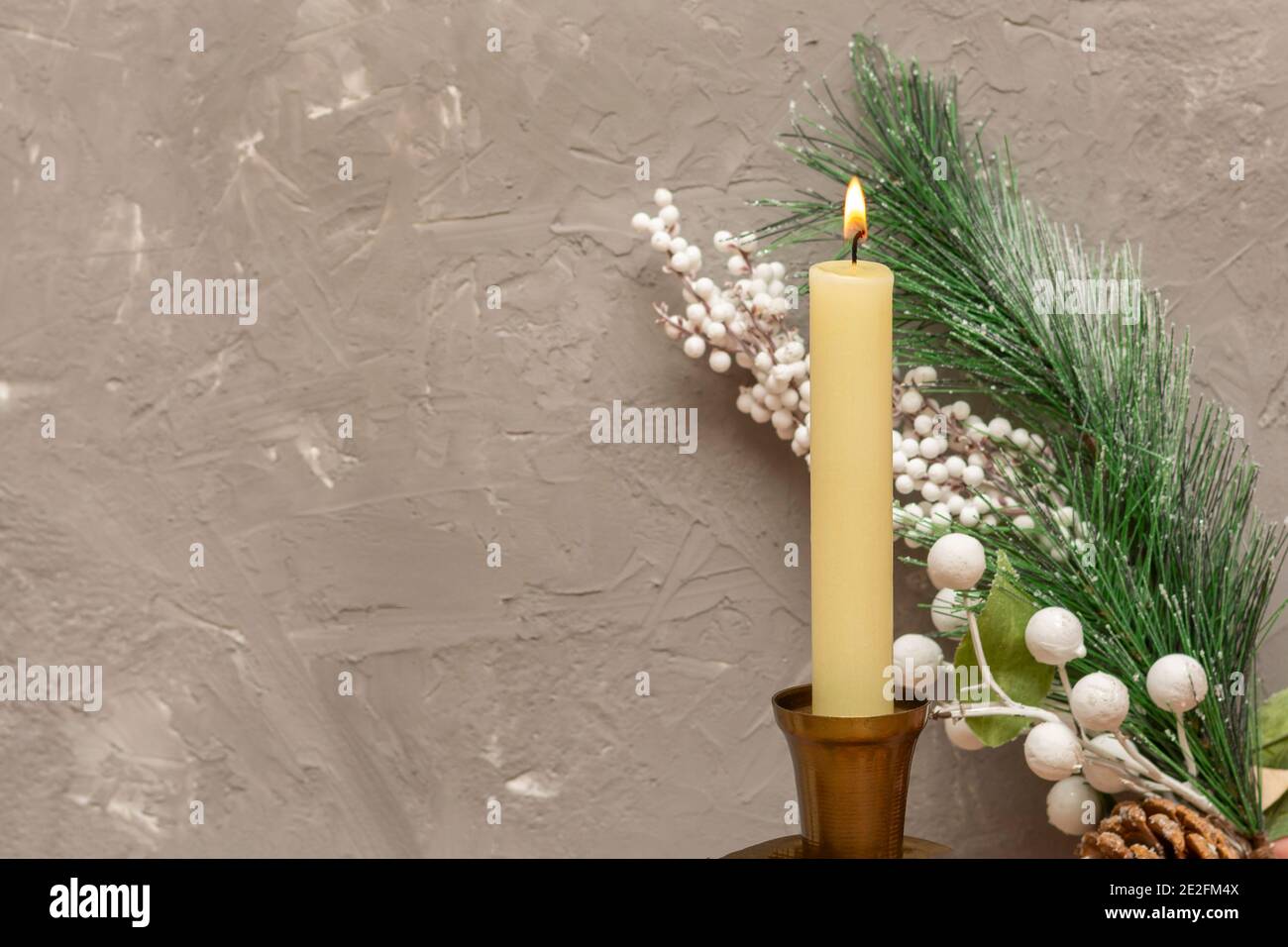 White candle with fire and branch of New Year tree on gray concrete wall. Selective focus, blurred background, copy space. Stock Photo
