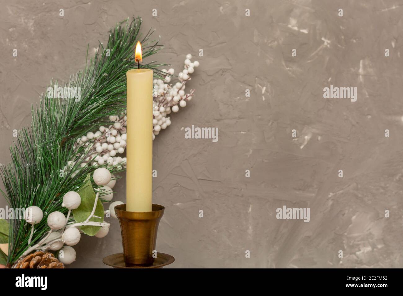 Fire of white candle against background of Christmas tree branch and gray concrete wall. Selective focus, blurred background, copy space. Stock Photo
