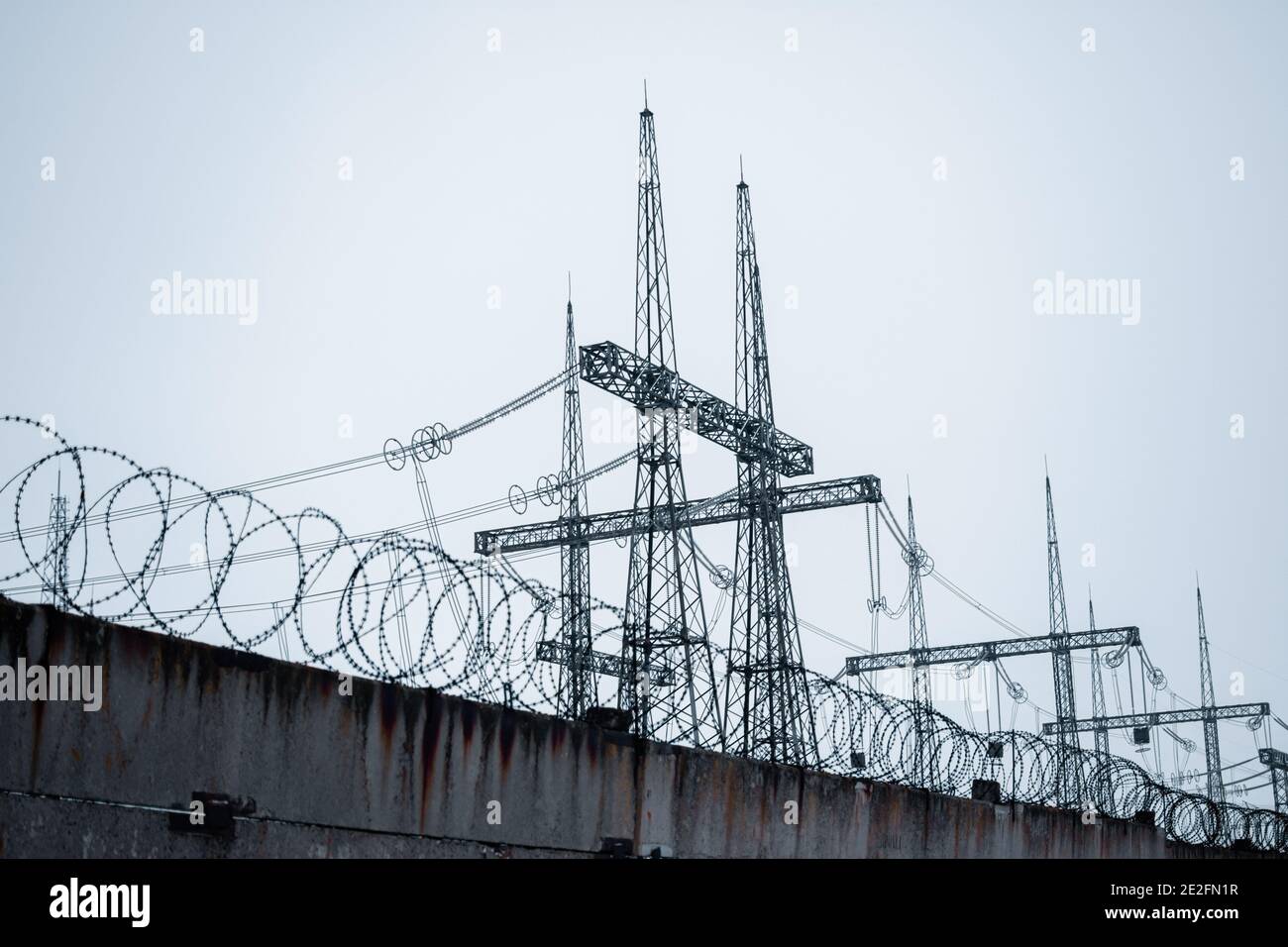 High-voltage power lines behind a fence with barbed wire. Stock Photo