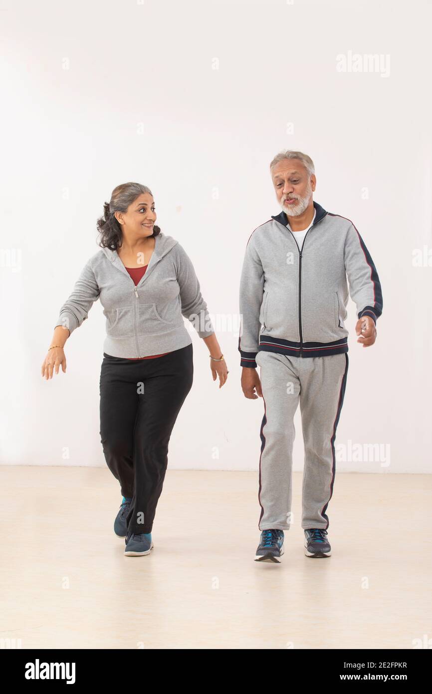 A SENIOR ADULT WOMAN HAPPILY LISTENING TO HER HUSBAND WHILE WALKING TOGETHER Stock Photo