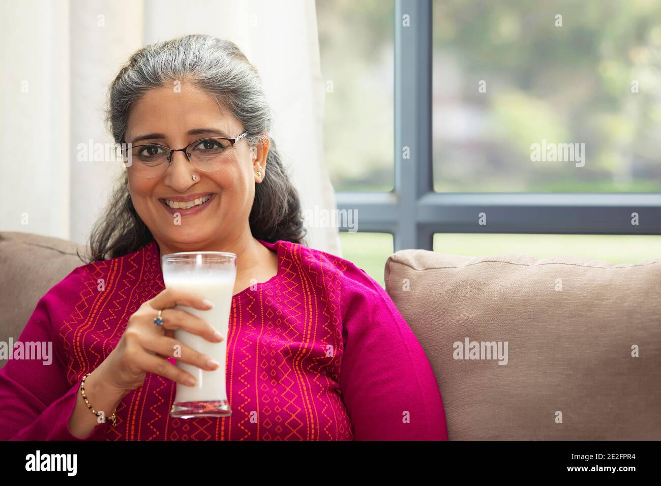 A HAPPY OLD WOMAN SITTING ON SOFA AND DRINKING MILK Stock Photo