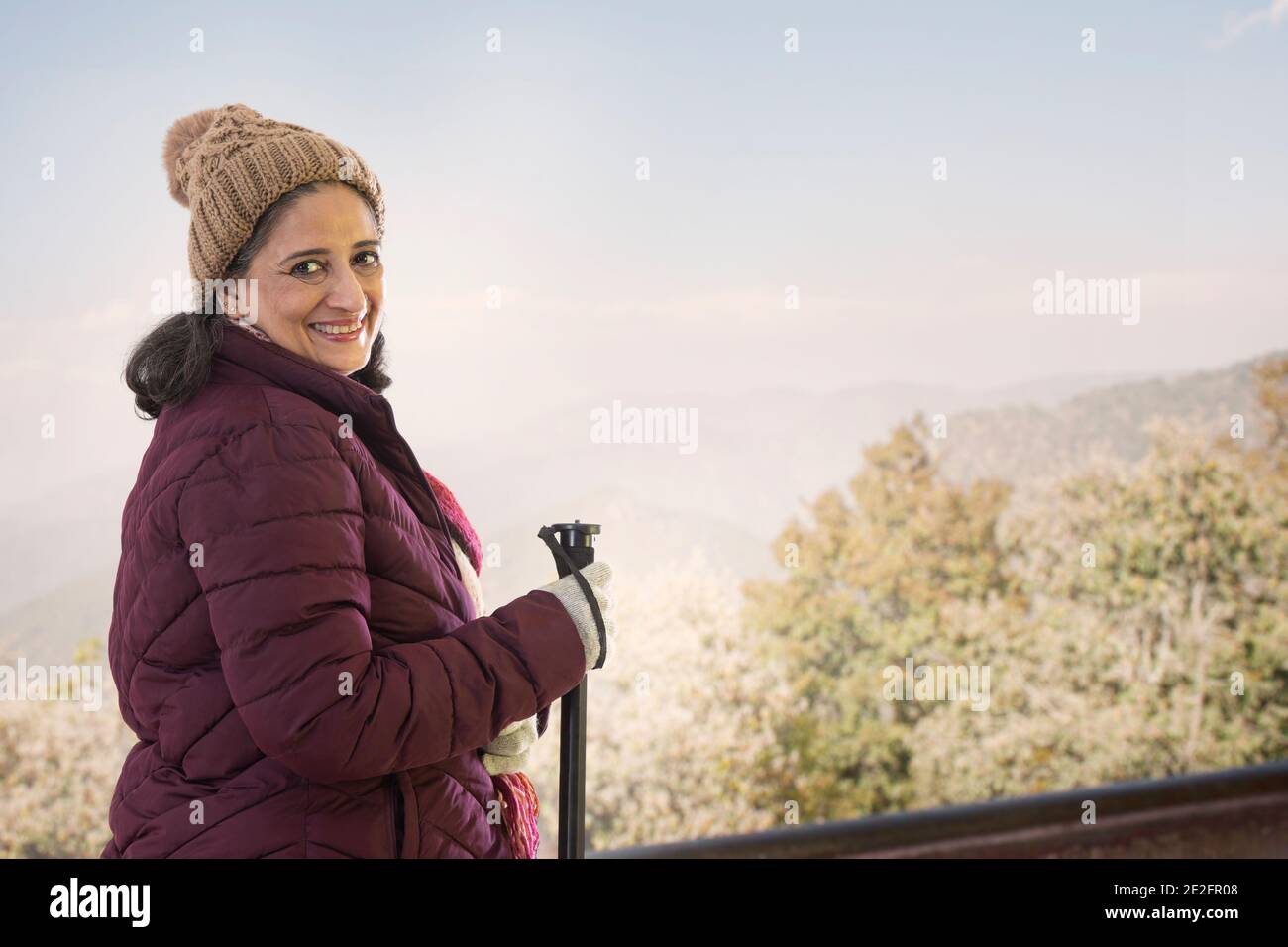 A SENIOR ADULT WOMAN HAPPILY LOOKING BEHIND WHILE TREKKING Stock Photo