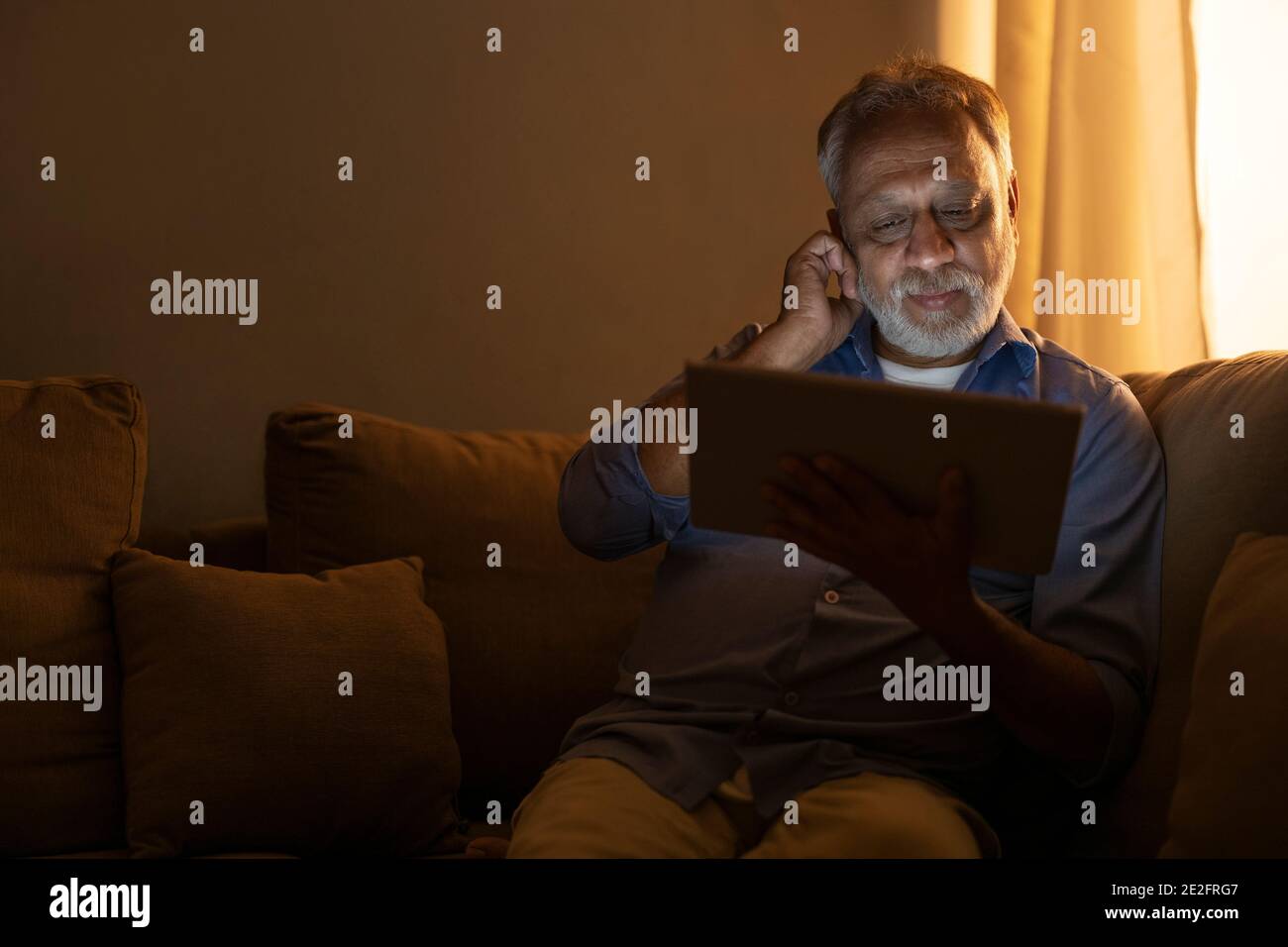 A SENIOR ADULT MAN SITTING AND USING DIGITAL TABLET Stock Photo