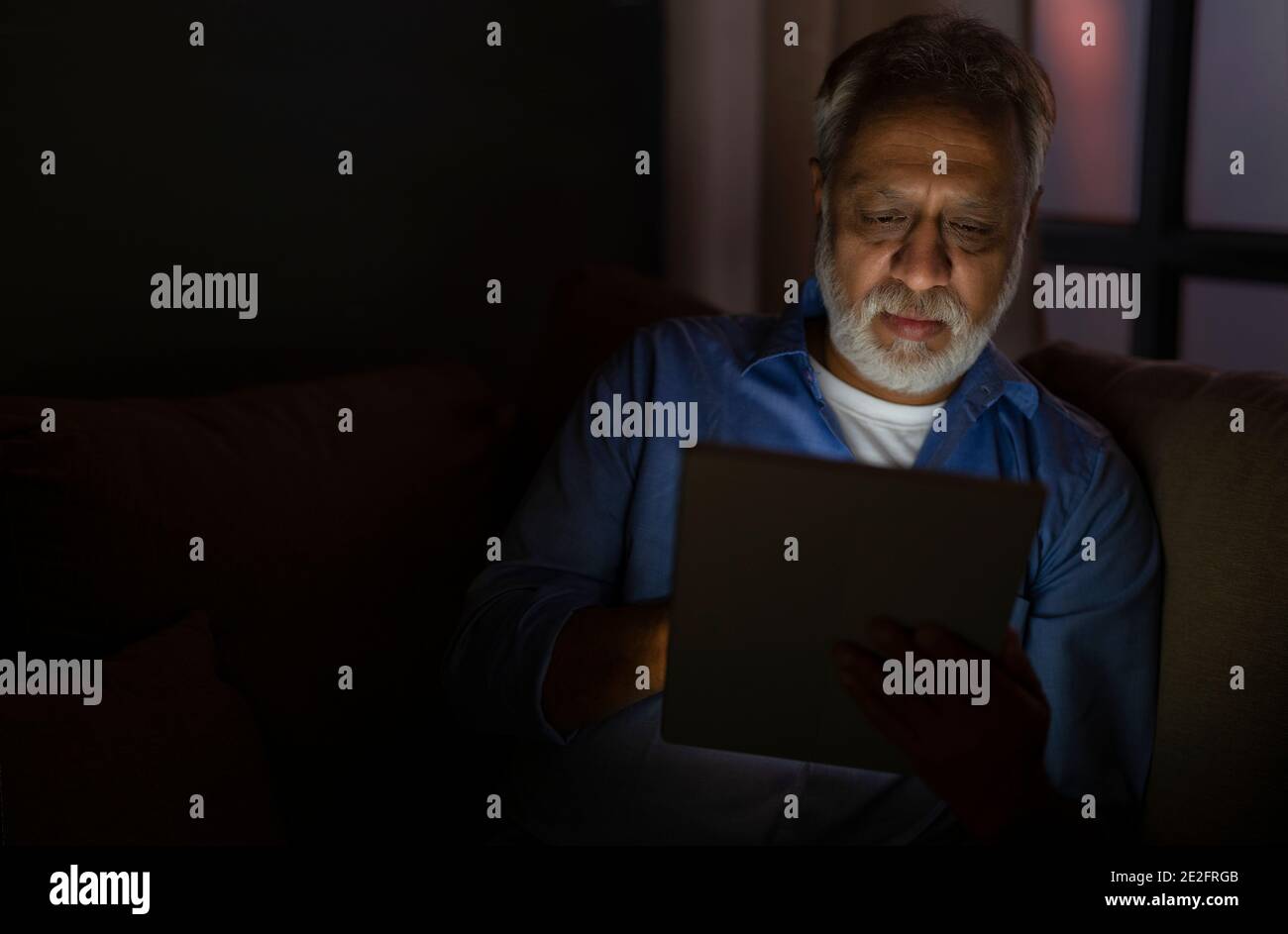 A SENIOR ADULT MAN USING DIGITAL TABLET AT NIGHT Stock Photo