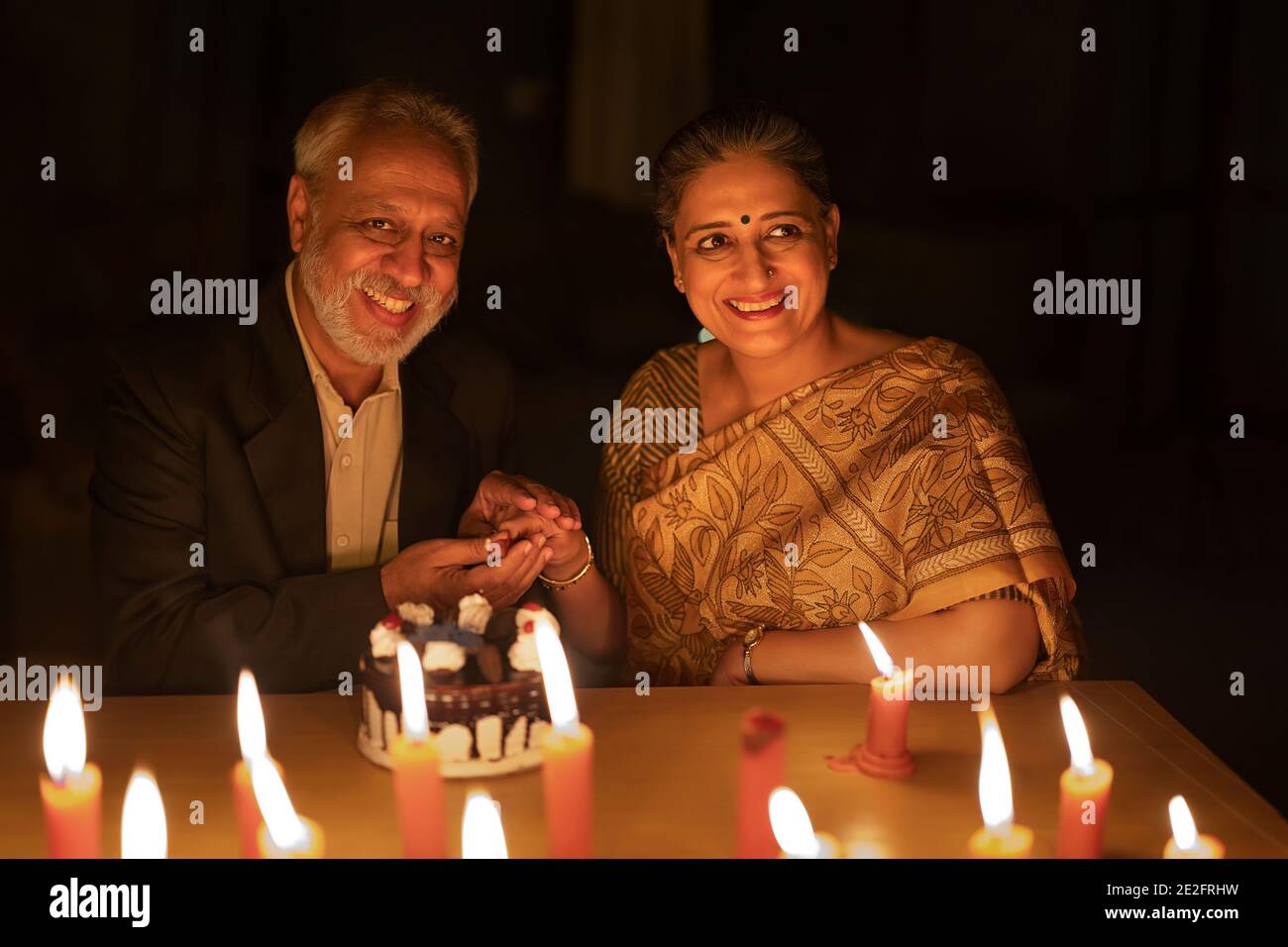 AN OLD COUPLE HAPPILY CUTTING CAKE ON THEIR ANNIVERSARY Stock Photo