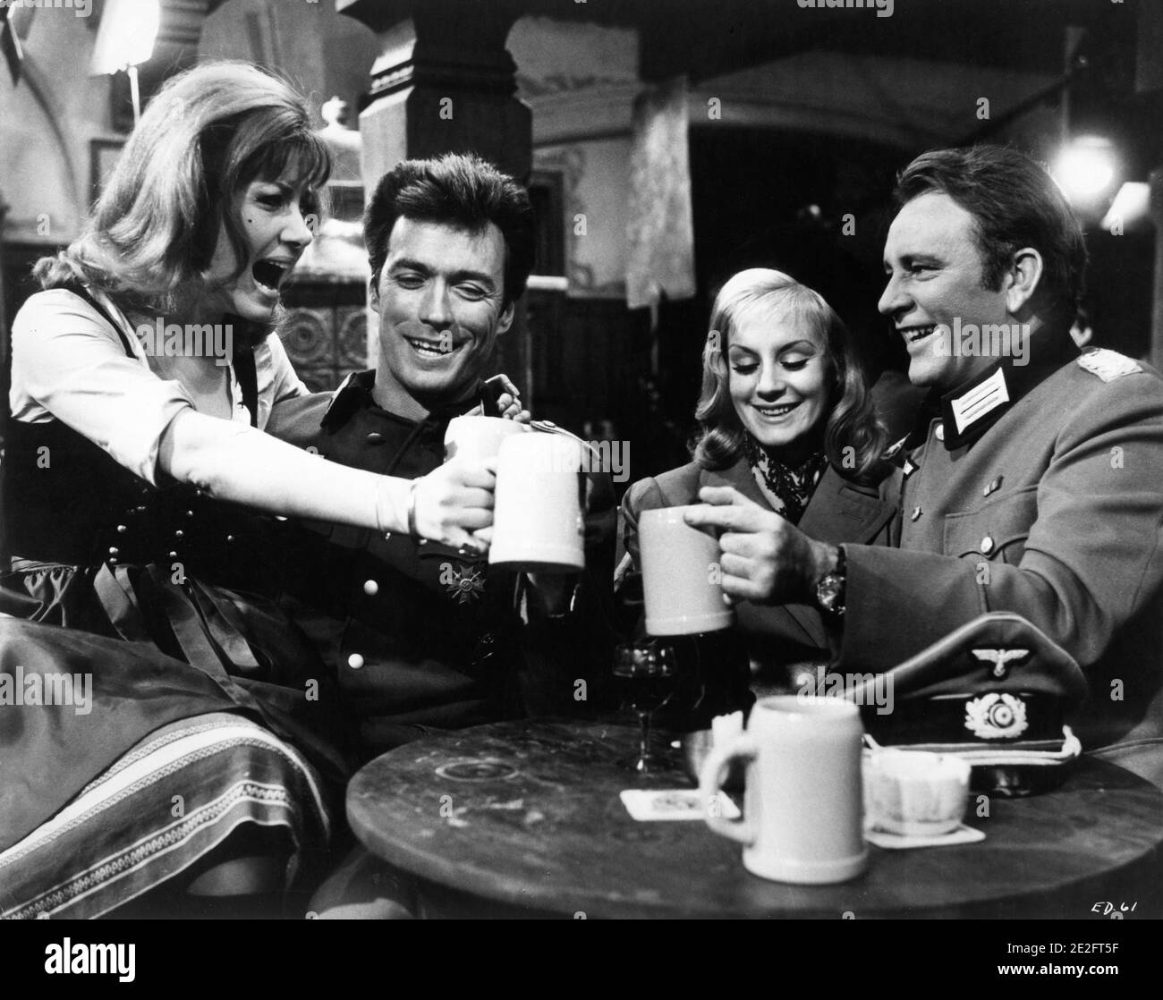 INGRID PITT CLINT EASTWOOD MARY URE and RICHARD BURTON on set candid portrait clinking beer mugs during filming of WHERE EAGLES DARE 1968 director BRIAN G. HUTTON story / screenplay Alistair MacLean music Ron Goodwin producers Elliot Kastner and Jerry Gershwin  Gershwin-Kastner Productions / Winkast Film Productions / Metro Goldwyn Mayer Stock Photo